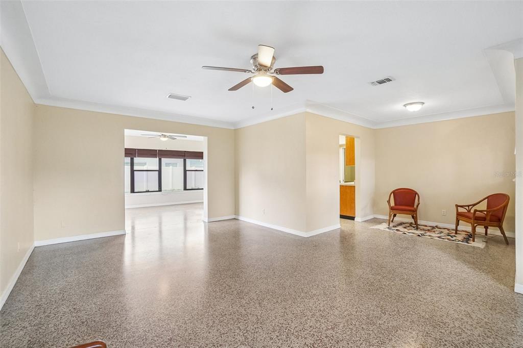 A spacious living area features light-colored walls, a ceiling fan, and speckled concrete flooring — 1421 TEMPLE STREET, CLEARWATER, FL