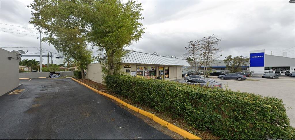 A low-rise commercial building with a metal roof sits behind a hedge and parking lot — 19301 NW 2ND AVENUE, MIAMI, FL