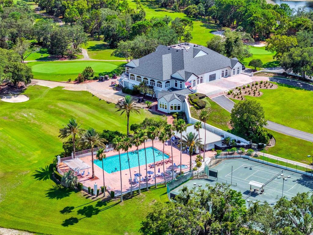 An aerial view shows a large clubhouse, a swimming pool, and tennis courts on a golf course — 9316 GENTLE BEN COURT, WEEKI WACHEE, FL