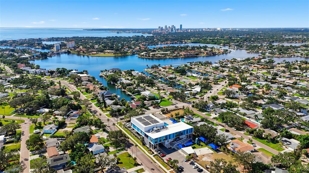 An aerial view shows a modern building surrounded by suburban houses, waterways, and a distant city — 4324 BAYSHORE BOULEVARD NE, ST PETERSBURG, FL