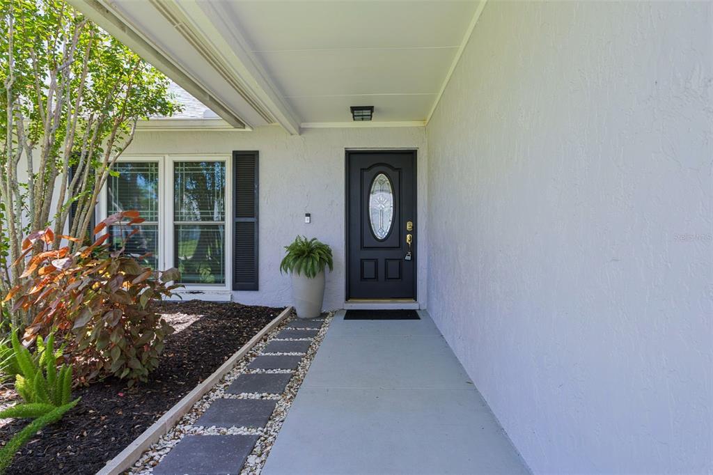 A concrete walkway leads to a black front door under a covered porch — 16117 PEBBLEBROOK DRIVE, TAMPA, FL