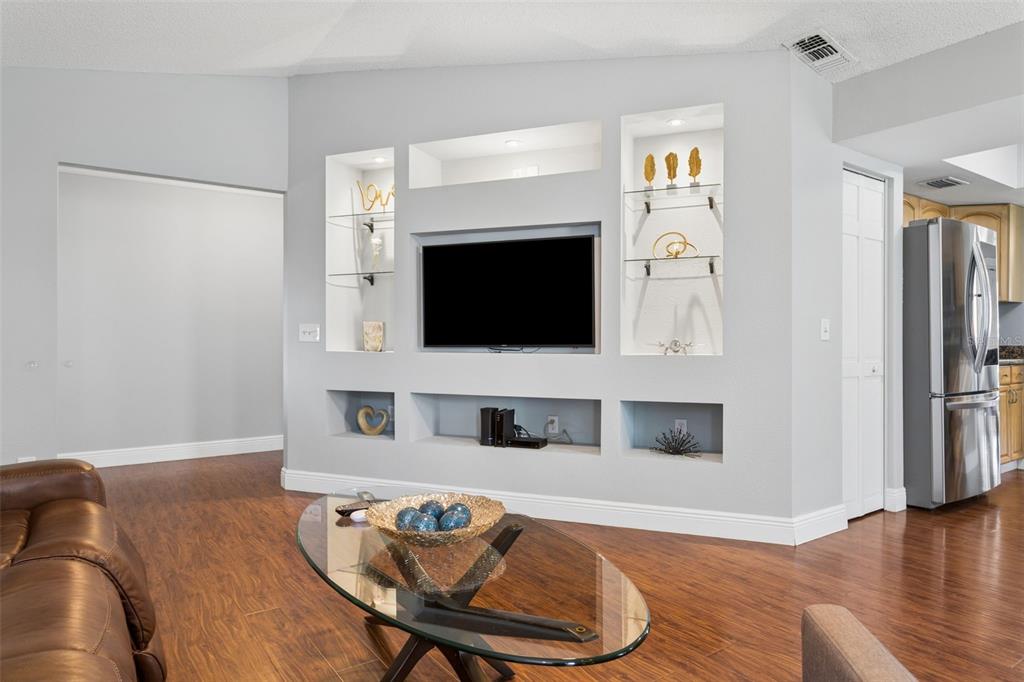 A living room features a built-in media wall with recessed shelving and a mounted television — 16117 PEBBLEBROOK DRIVE, TAMPA, FL
