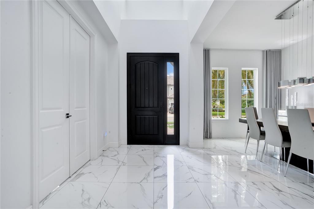 A bright entryway features white marble floors, a black front door, and an adjacent dining area — 16548 RAVEN ROCK PLACE, WINTER GARDEN, FL