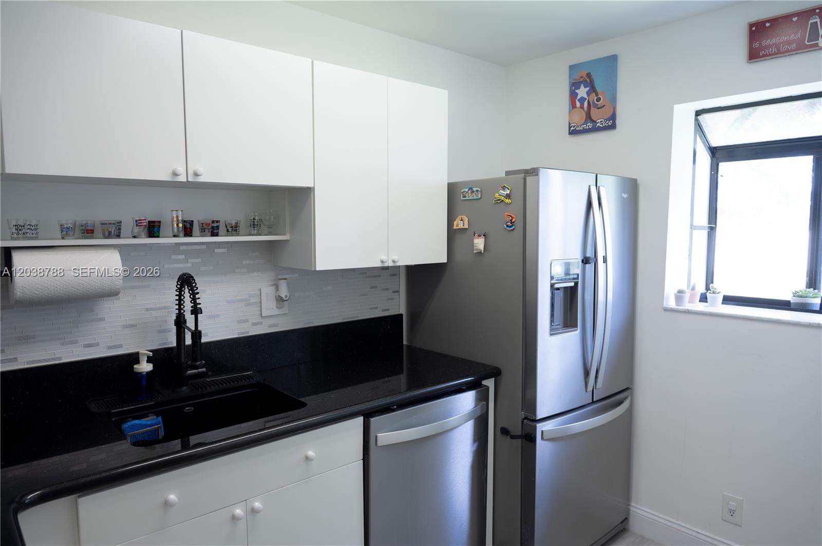A kitchen features white cabinets, black countertops, stainless steel appliances, and a tiled backsplash — 508 Gardens Dr # 202, Pompano Beach FL 33069, POMPANO BEACH, FL