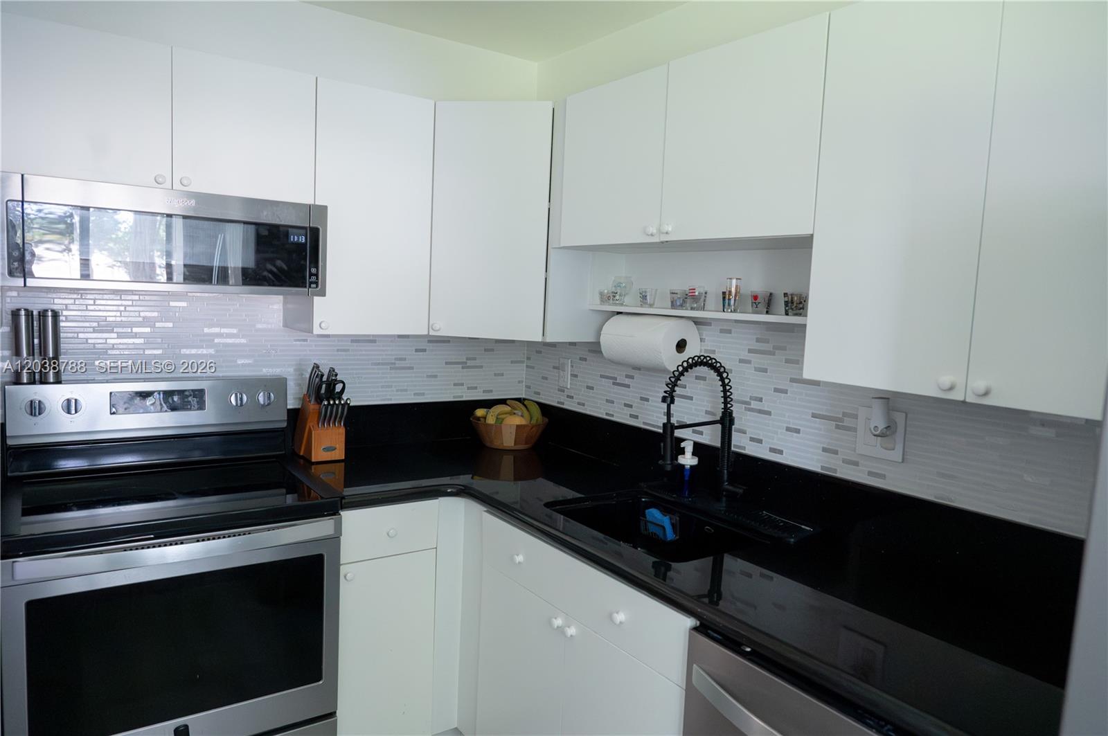 A kitchen features white cabinets, black countertops, stainless steel appliances, and a tiled backsplash — 508 Gardens Dr # 202, Pompano Beach FL 33069, POMPANO BEACH, FL