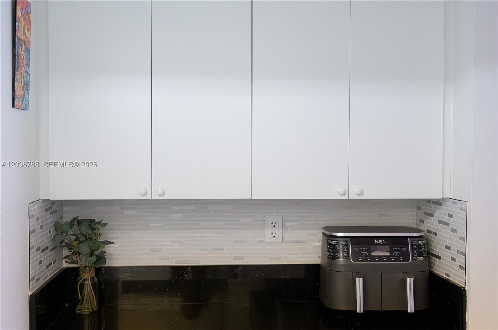 A kitchen counter features black stone, a tiled backsplash, white cabinets, and a Ninja appliance — 508 Gardens Dr # 202, Pompano Beach FL 33069, POMPANO BEACH, FL