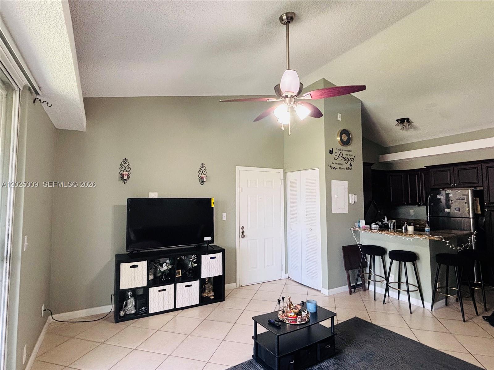 A living room features a television console, a ceiling fan, and an adjacent kitchen bar — 951 Lyons Rd # 6206, Coconut Creek FL 33063, COCONUT CREEK, FL