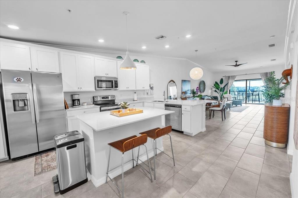 A modern kitchen with white cabinets, stainless steel appliances, and an island with bar stools — 5711 PALMER CIRCLE UNIT 206, BRADENTON, FL