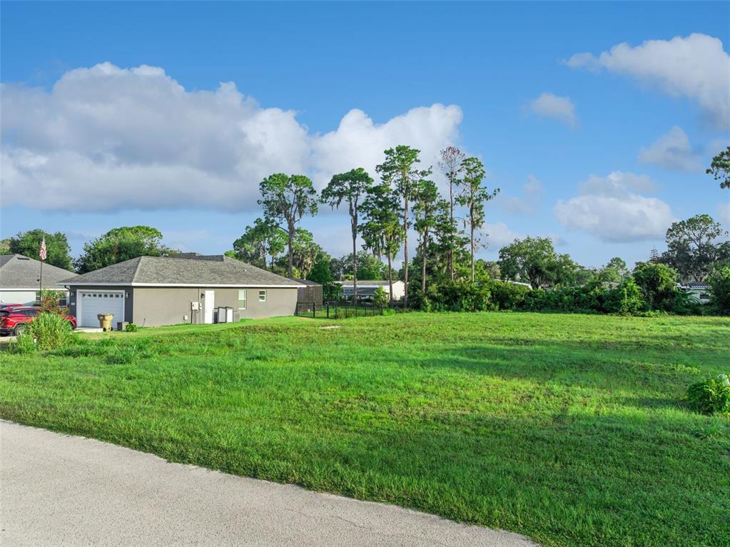 A grassy vacant lot sits next to a single-story house with a gray exterior — 12045 EAGLE POINT COURT, LEESBURG, FL