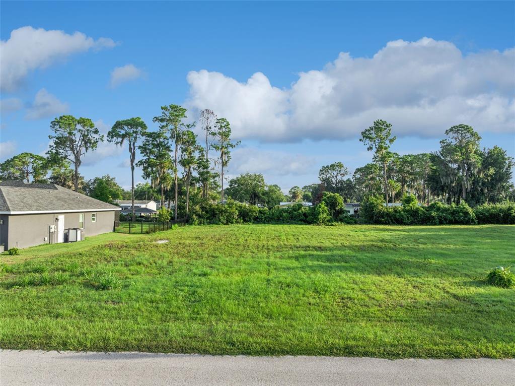 A vacant, grassy residential lot sits adjacent to a gray house under a blue sky — 12045 EAGLE POINT COURT, LEESBURG, FL