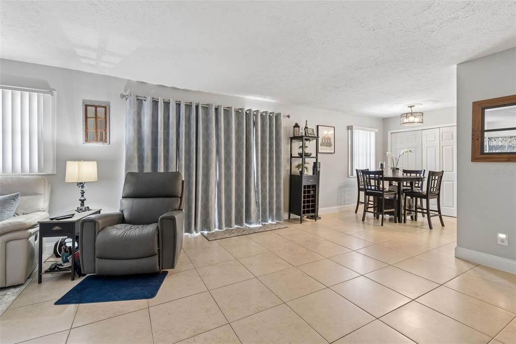 A living room and dining area with tile floors, a recliner, and sliding glass doors — 13765 JUNIPER BLOSSOM DRIVE UNIT 101, TAMPA, FL