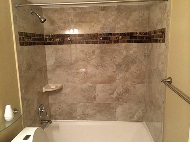 A bathroom features a white bathtub with a showerhead and beige marble-tiled walls — 363 W Camino Real # 5, Boca Raton FL 33432, BOCA RATON, FL