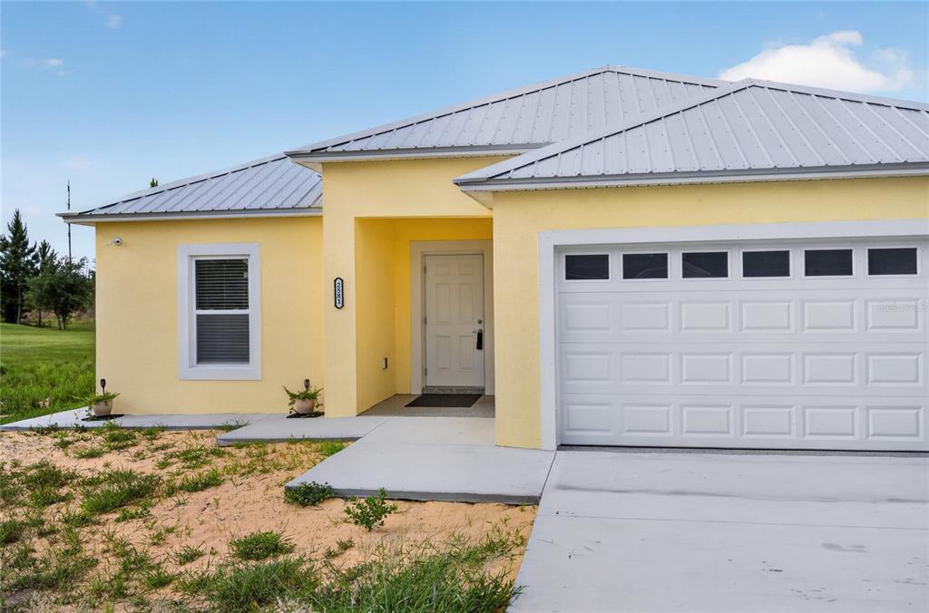 A yellow single-story house with a white metal roof and a two-car garage — 2581 POINCIANA DRIVE, INDIAN LAKE ESTATES, FL
