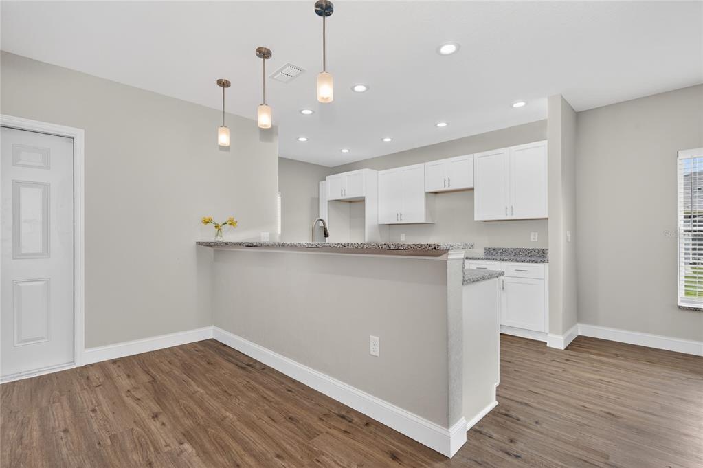 A kitchen with white cabinets, granite countertops, and a breakfast bar overlooking a dining area — 2581 POINCIANA DRIVE, INDIAN LAKE ESTATES, FL