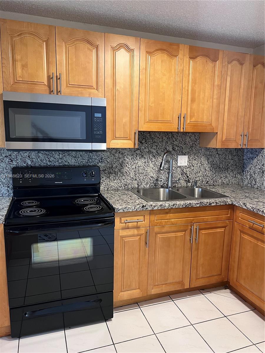 A kitchen features light wood cabinets, granite countertops, a black stove, and a stainless microwave — 2750 W 76th St # 208, Hialeah FL 33016, HIALEAH, FL