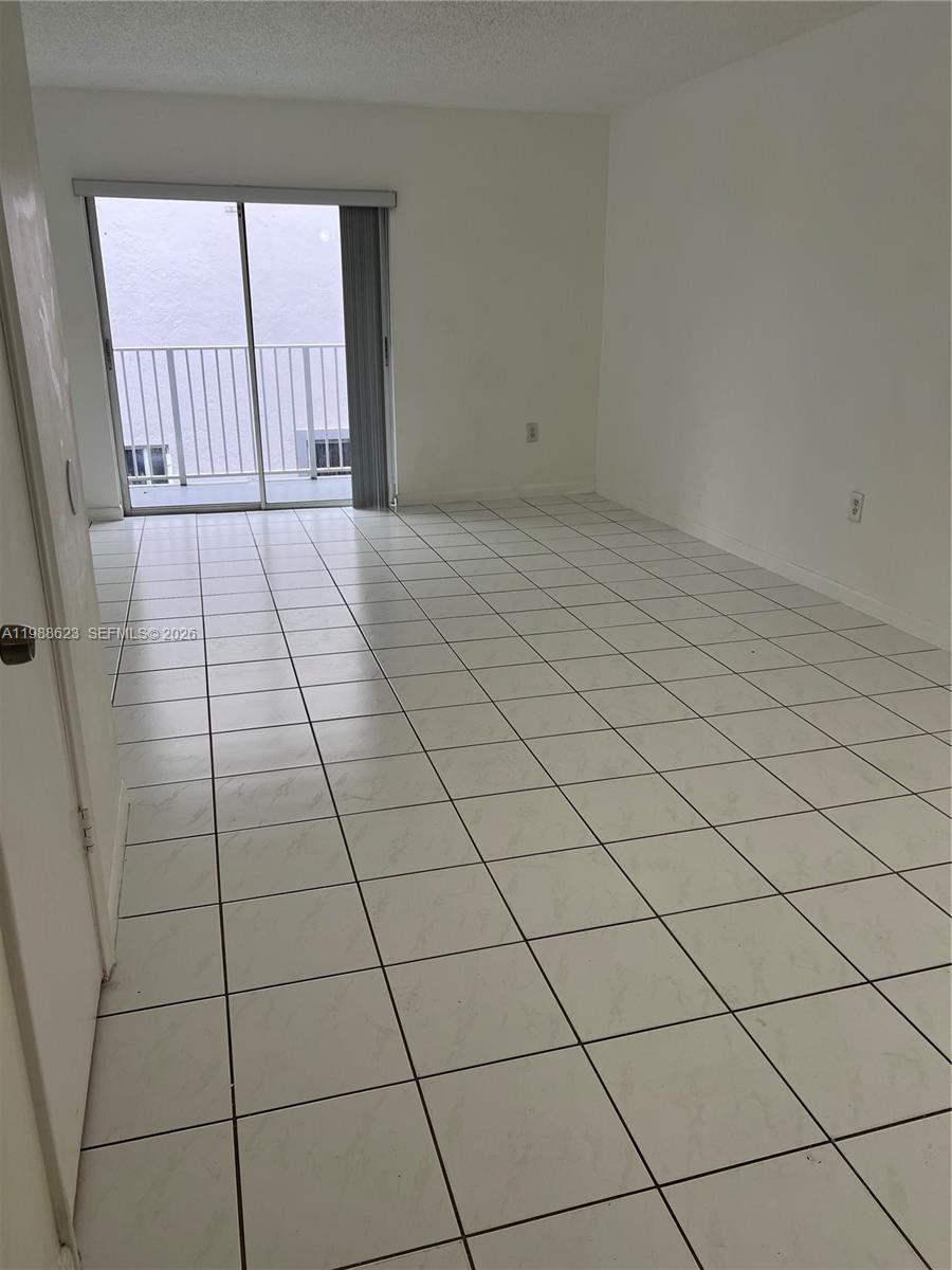 An empty room features white tiled floors, plain white walls, and a sliding glass door — 2750 W 76th St # 208, Hialeah FL 33016, HIALEAH, FL