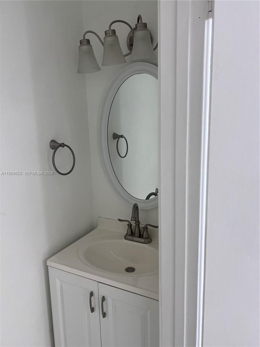 A small bathroom features a white vanity, an oval mirror, and a three-light fixture — 2750 W 76th St # 208, Hialeah FL 33016, HIALEAH, FL
