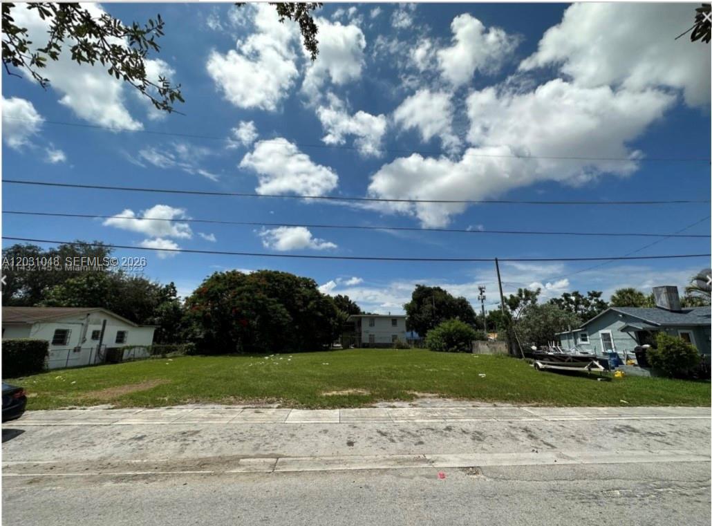A vacant, grassy residential lot sits between two existing houses under a cloudy blue sky — 1624 NW 60th St, Miami FL 33142, MIAMI, FL