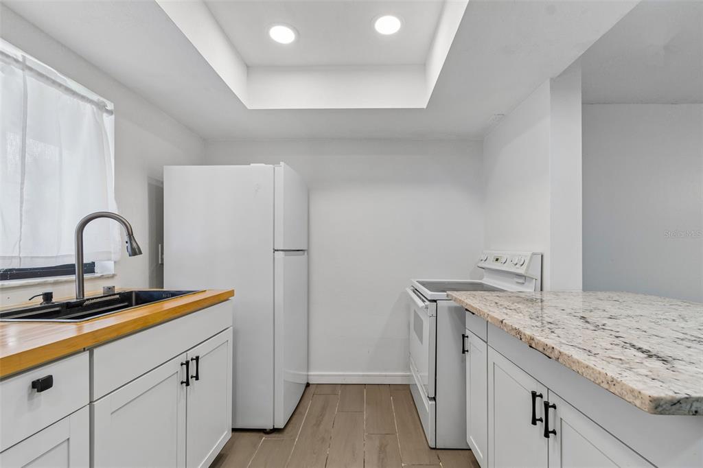 A kitchen features white cabinets, a wood countertop, a granite island, and white appliances — 3911 OAK LIMB COURT, TAMPA, FL
