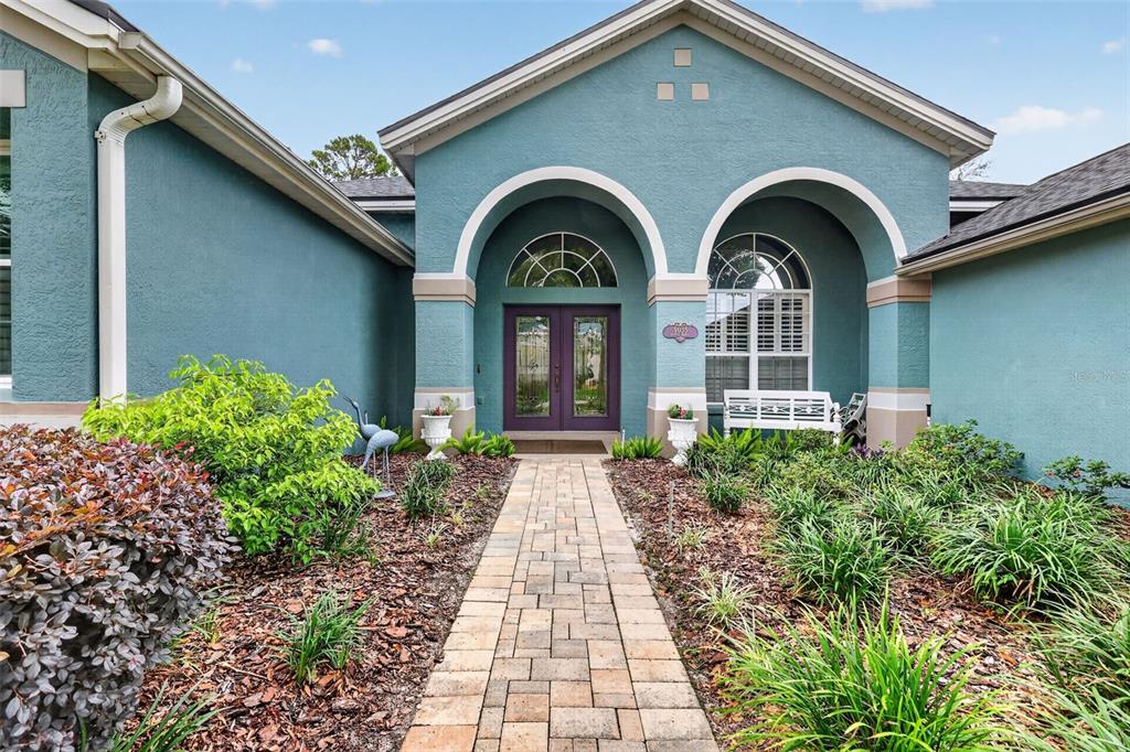A teal house exterior features a stone walkway leading to a double-door arched entryway — 9035 LAUREL RIDGE DRIVE, MOUNT DORA, FL