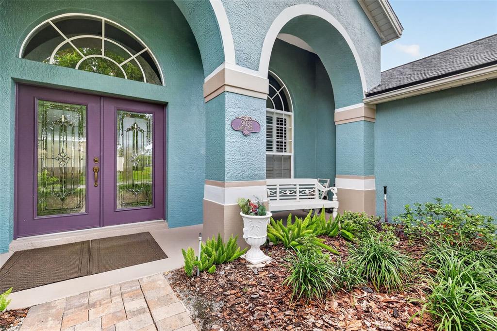 A teal house exterior features a purple double front door and a white bench — 9035 LAUREL RIDGE DRIVE, MOUNT DORA, FL