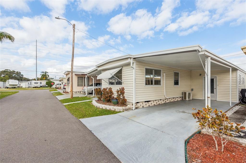 A single-story mobile home with a carport, light siding, and a small landscaped garden bed — 1600 N OLD COACHMAN ROAD UNIT 311, CLEARWATER, FL