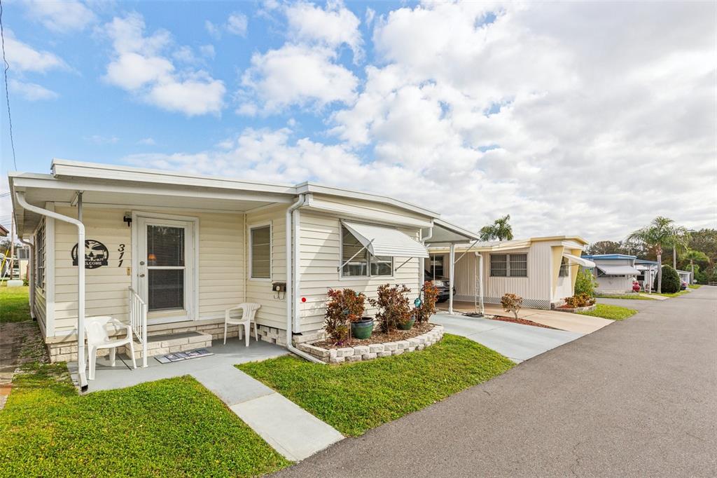 A light-colored mobile home features a covered entryway, a small front lawn, and a carport — 1600 N OLD COACHMAN ROAD UNIT 311, CLEARWATER, FL