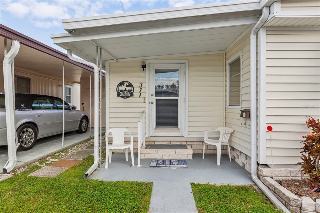 A small covered front porch features two white plastic chairs and a storm door — 1600 N OLD COACHMAN ROAD UNIT 311, CLEARWATER, FL