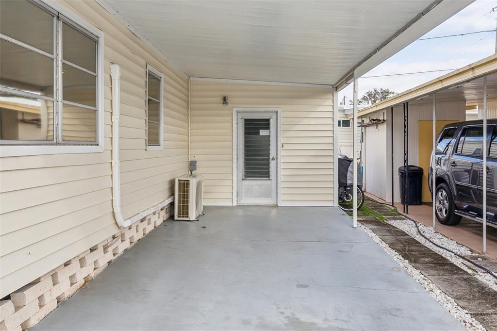 A covered carport area features light-colored siding, a glass-paneled door, and a concrete floor — 1600 N OLD COACHMAN ROAD UNIT 311, CLEARWATER, FL