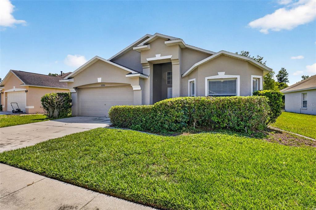 A single-story suburban house with a beige exterior, a two-car garage, and a manicured hedge — 1235 KATAHDIN COURT, WESLEY CHAPEL, FL
