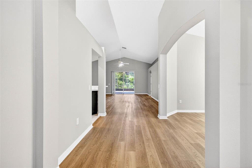 A view through a hallway with light wood flooring toward a living area with vaulted ceilings — 1235 KATAHDIN COURT, WESLEY CHAPEL, FL