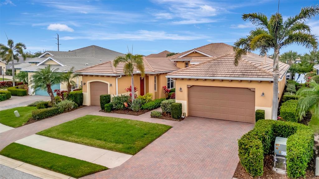 A tan, single-story house with a tile roof, two-car garage, and landscaped front yard — 1022 KESTREL COURT, BRADENTON, FL