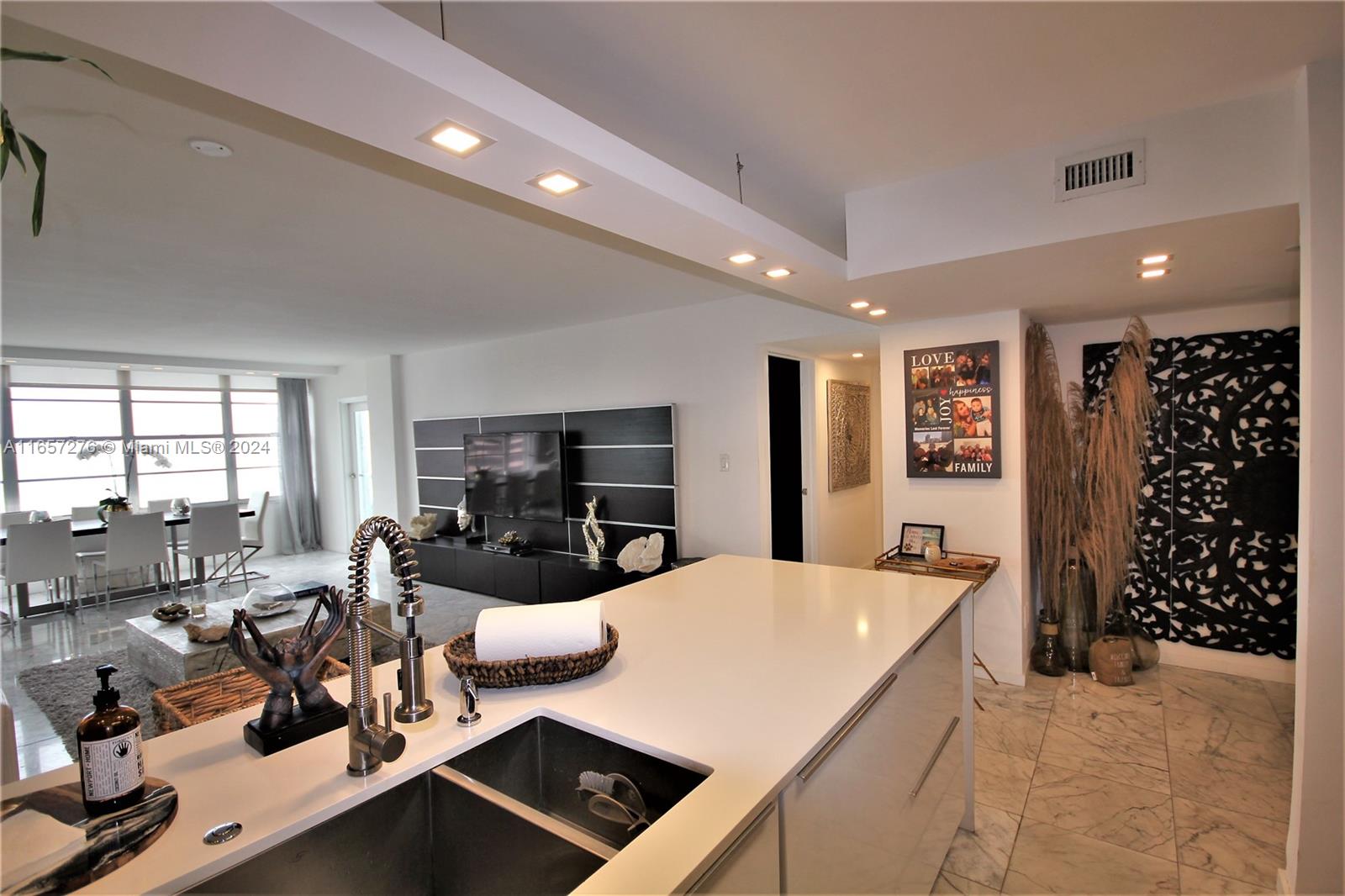 A modern kitchen island with a sink overlooks an open-concept living and dining area — 5151 Collins Ave # 933, Miami Beach FL 33140, MIAMI BEACH, FL