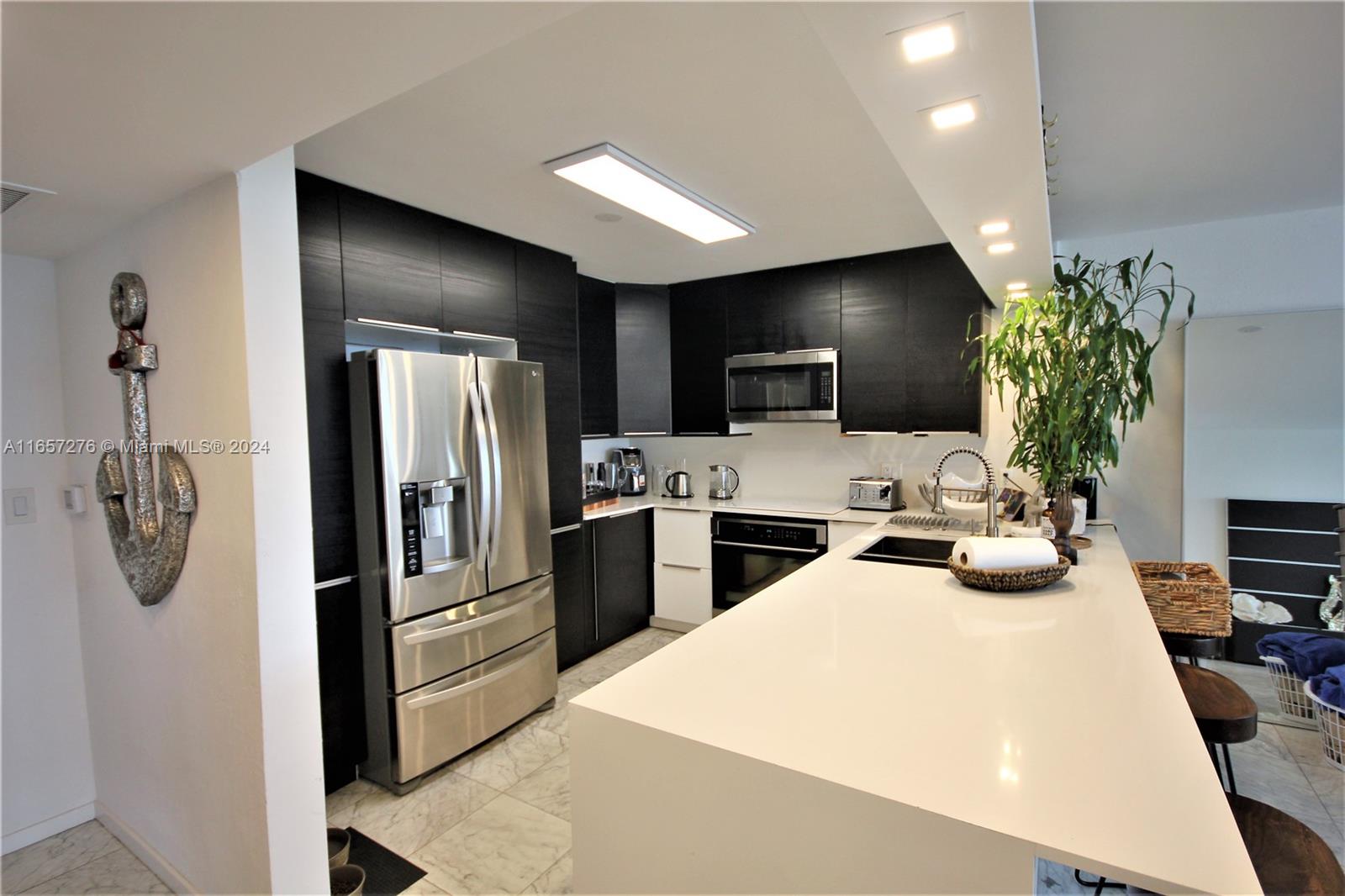 A modern kitchen features dark cabinetry, stainless steel appliances, and a large white quartz island — 5151 Collins Ave # 933, Miami Beach FL 33140, MIAMI BEACH, FL