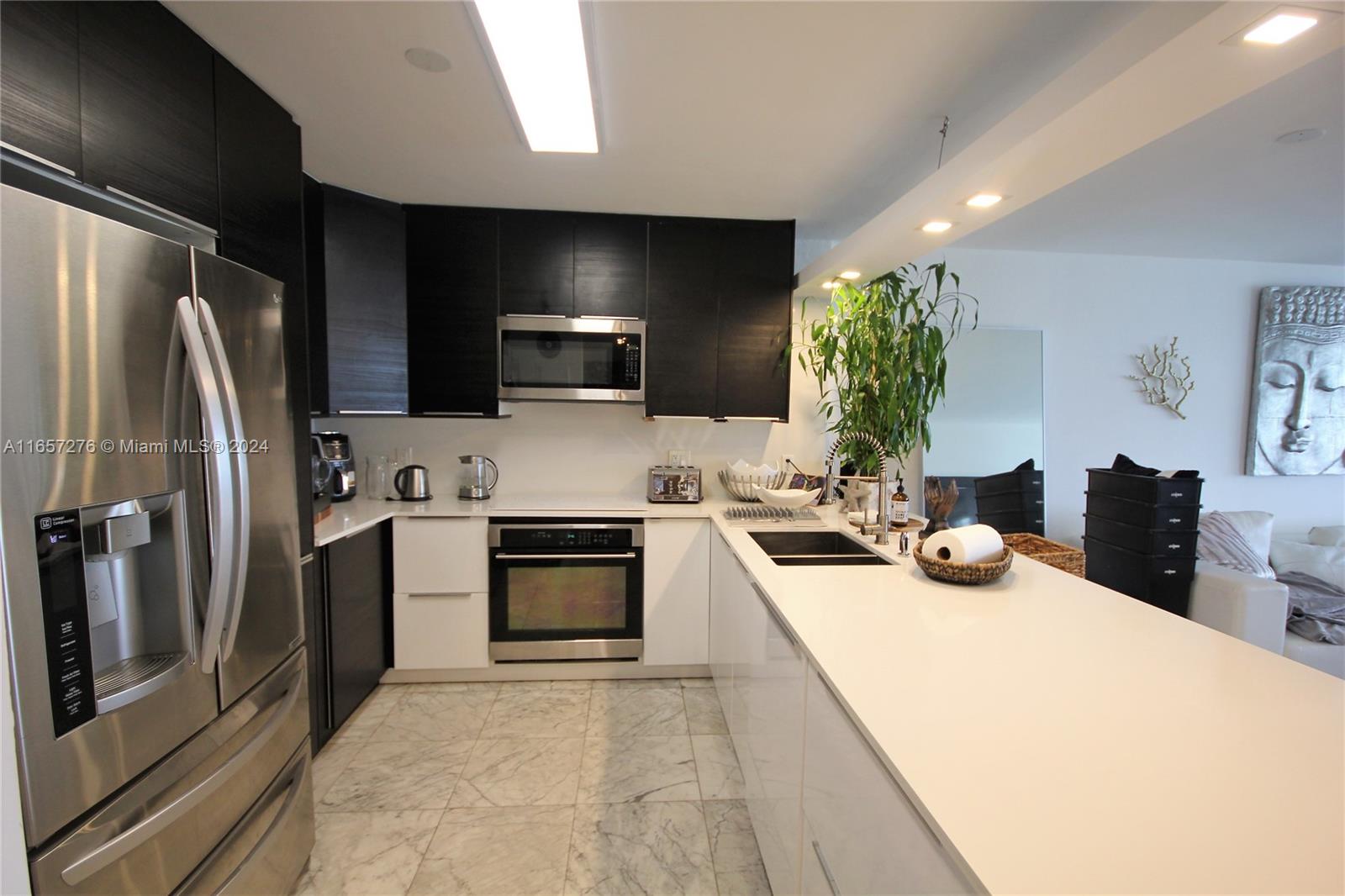 A modern kitchen features black upper cabinets, white lower cabinets, stainless steel appliances, and marble flooring — 5151 Collins Ave # 933, Miami Beach FL 33140, MIAMI BEACH, FL