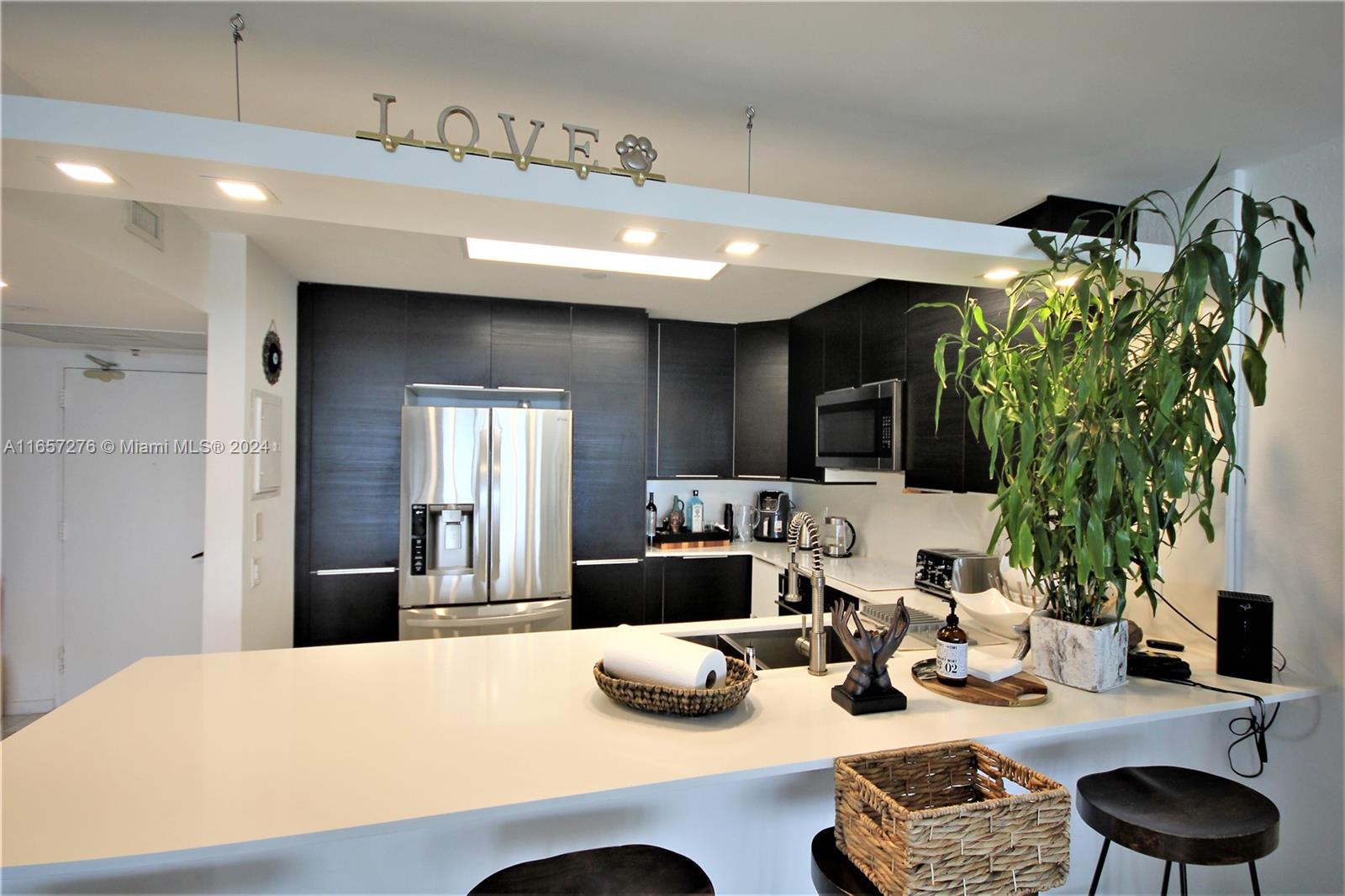 A modern kitchen features dark cabinetry, white countertops, a central island, and a large potted plant — 5151 Collins Ave # 933, Miami Beach FL 33140, MIAMI BEACH, FL