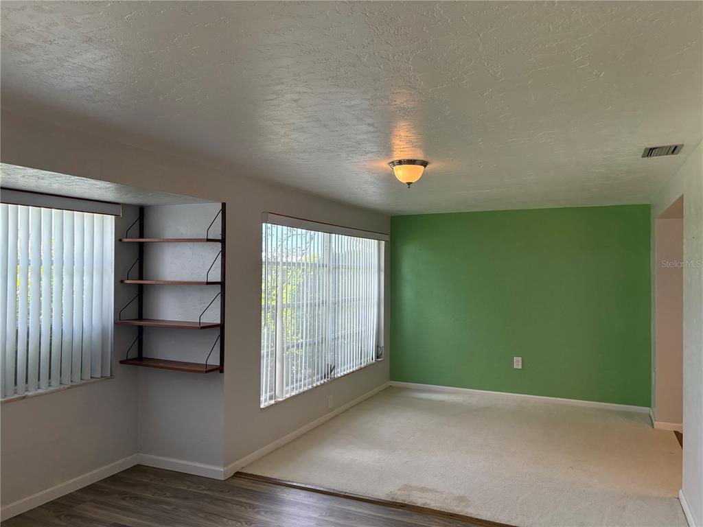 A living room features a green accent wall, beige carpeting, and built-in wooden shelves — 3276 BRUNSWICK LANE UNIT 705, SARASOTA, FL