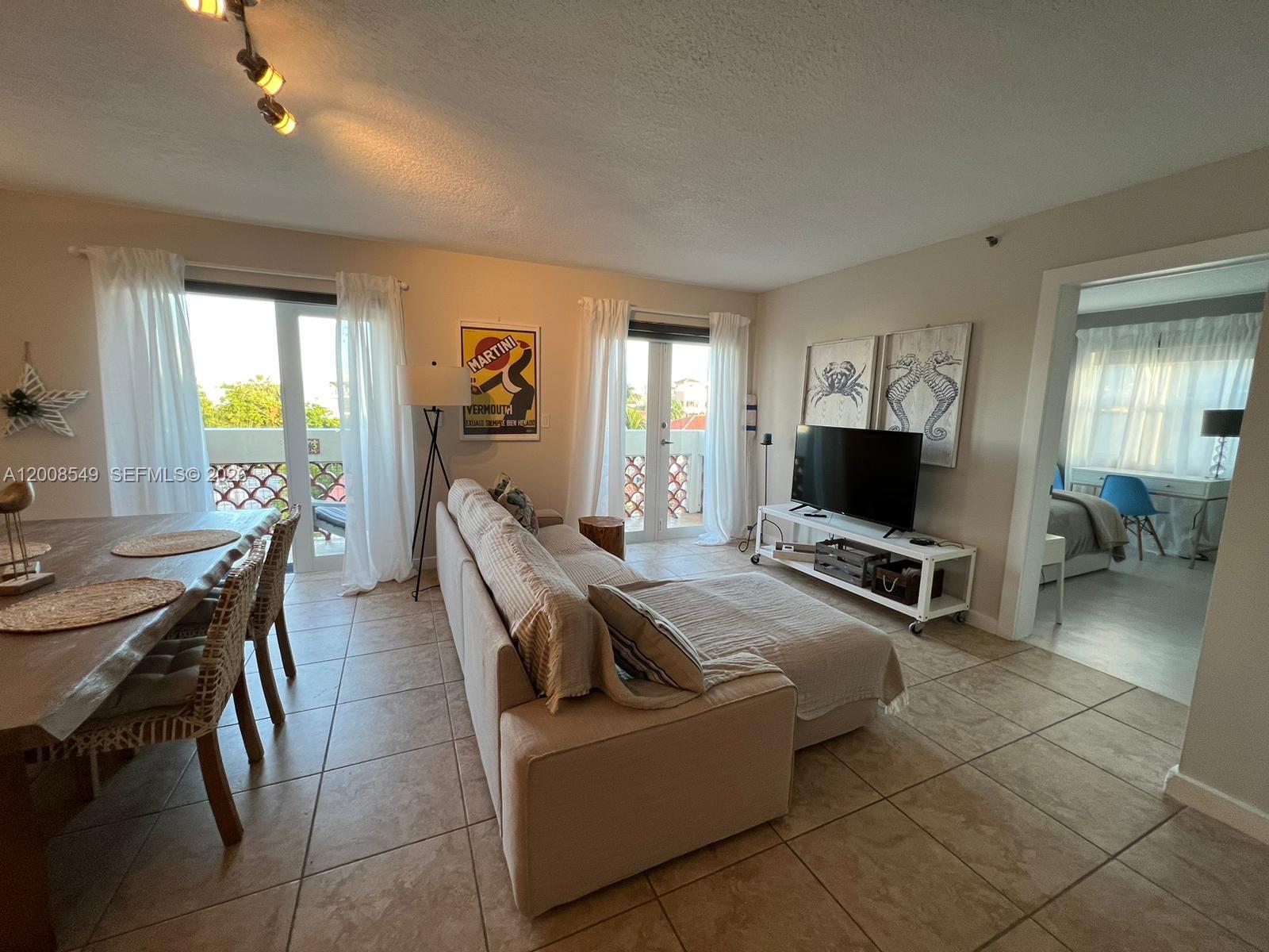A living room with tile floors, a sectional sofa, a dining area, and balcony access — 227 Michigan Ave # 502, Miami Beach FL 33139, MIAMI BEACH, FL