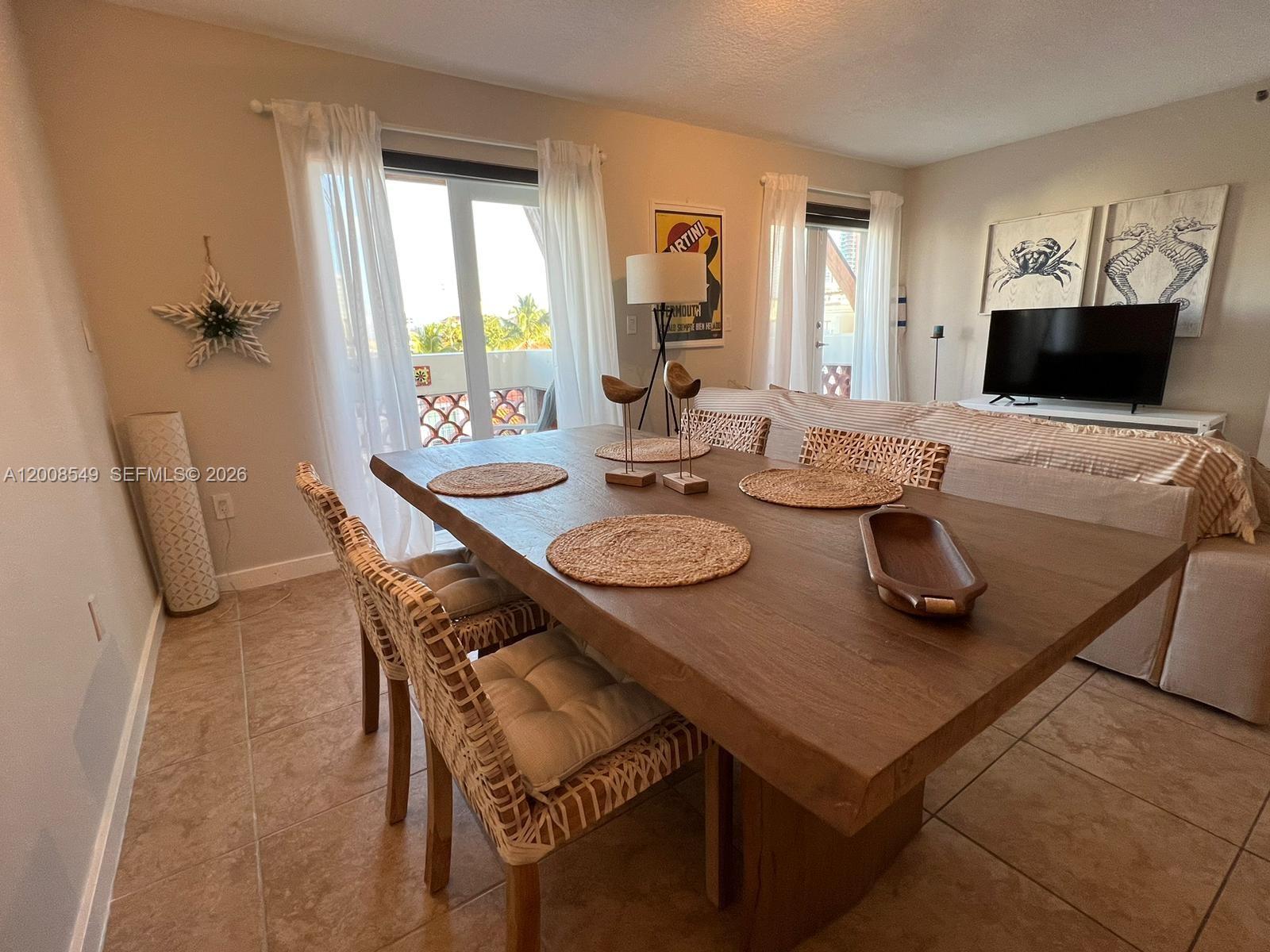 A dining room features a wooden table, woven chairs, and a television in the background — 227 Michigan Ave # 502, Miami Beach FL 33139, MIAMI BEACH, FL