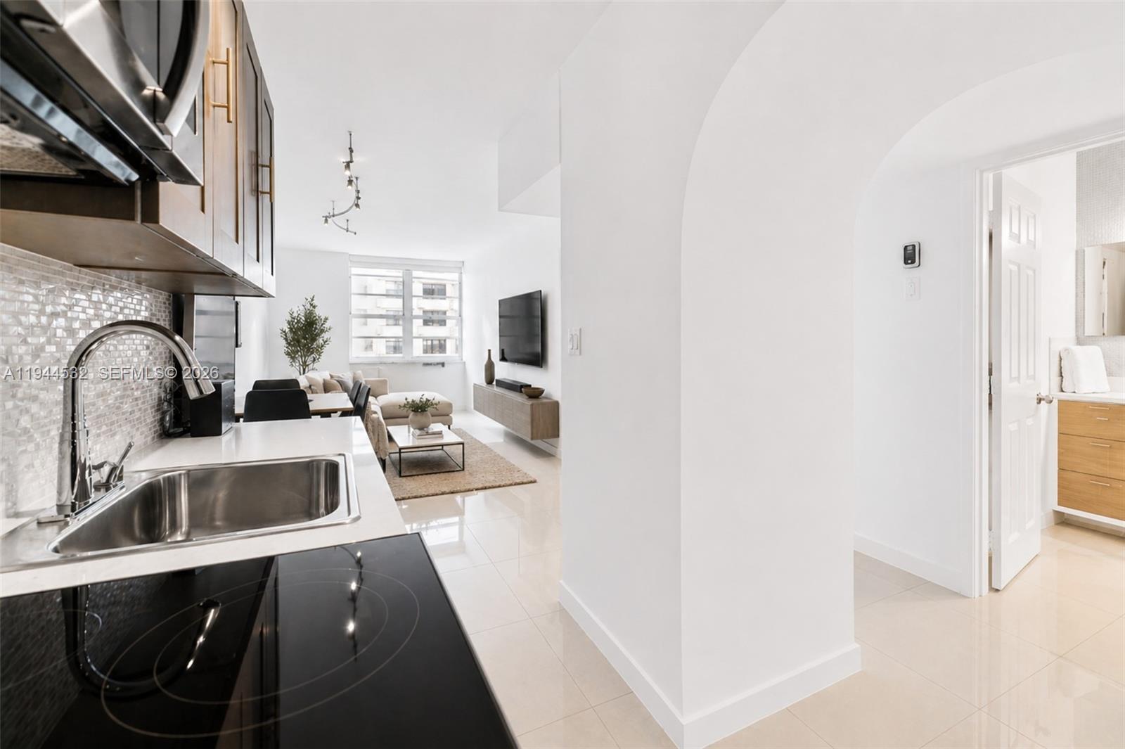 A modern kitchen overlooks a living area with a white arched entryway to the right — 100 Lincoln Rd # 501, Miami Beach FL 33139, MIAMI BEACH, FL