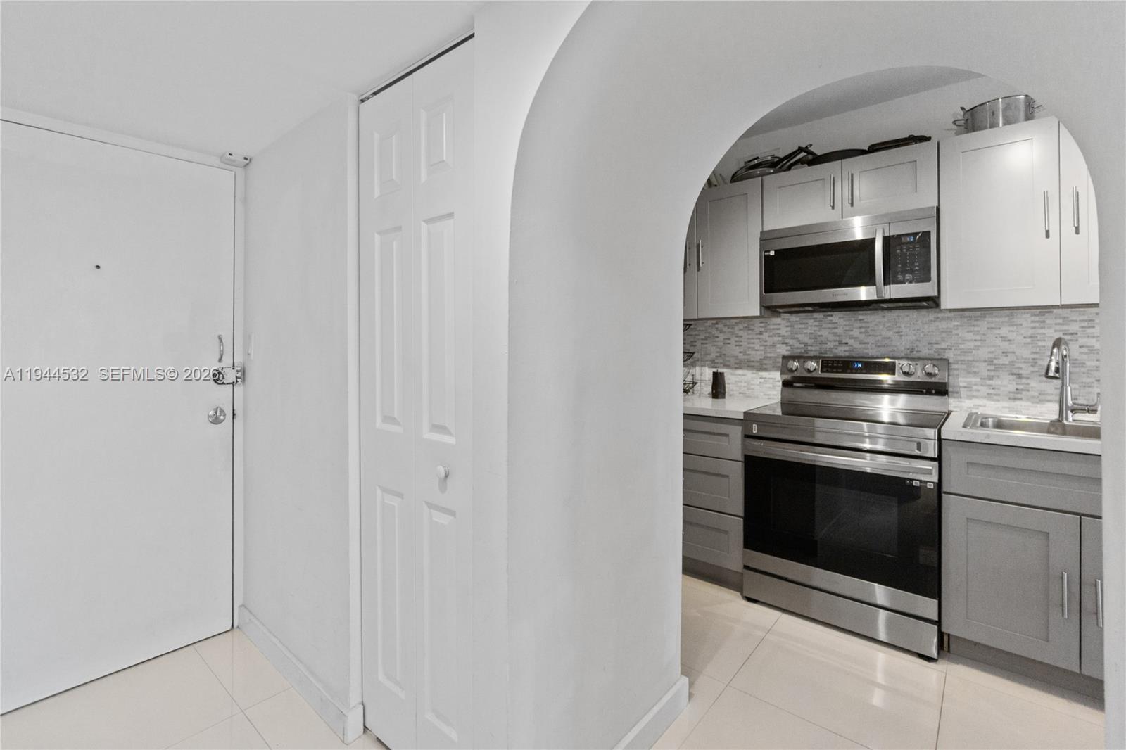 A white door and a closet lead to a kitchen with gray cabinets and appliances — 100 Lincoln Rd # 501, Miami Beach FL 33139, MIAMI BEACH, FL