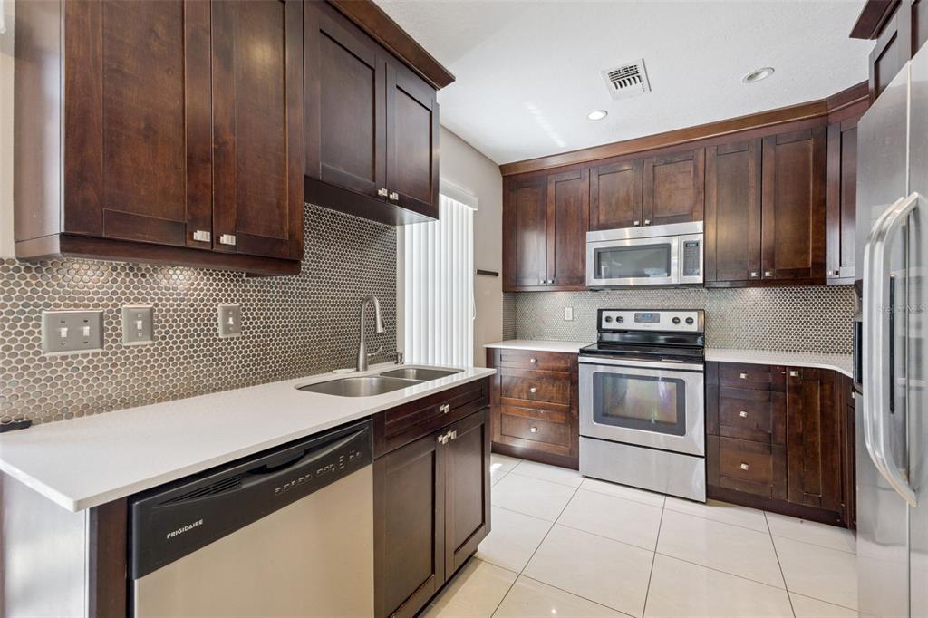 A kitchen features dark wood cabinets, stainless steel appliances, white countertops, and a mosaic backsplash — 3023 RIO GRANDE TRAIL UNIT 3023, KISSIMMEE, FL