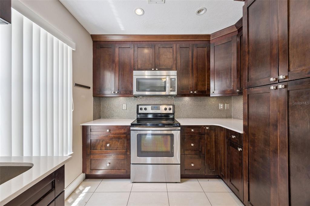 A kitchen features dark wood cabinets, stainless steel appliances, white countertops, and a mosaic backsplash — 3023 RIO GRANDE TRAIL UNIT 3023, KISSIMMEE, FL