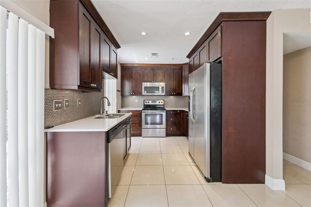 A kitchen features dark wood cabinets, stainless steel appliances, white countertops, and light tile flooring — 3023 RIO GRANDE TRAIL UNIT 3023, KISSIMMEE, FL