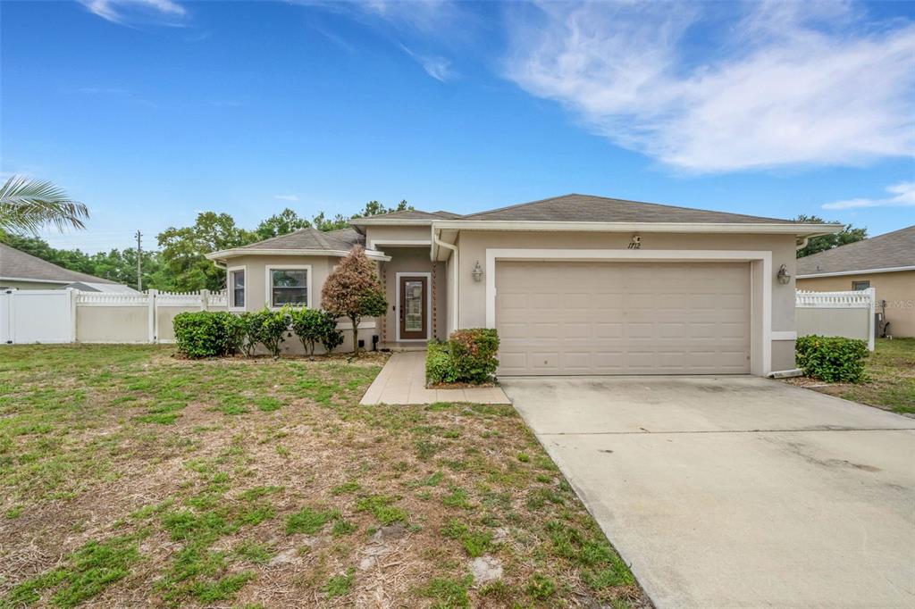 A single-story house with a beige exterior, a two-car garage, and a front walkway — 1712 CHARMI DRIVE, LAKELAND, FL