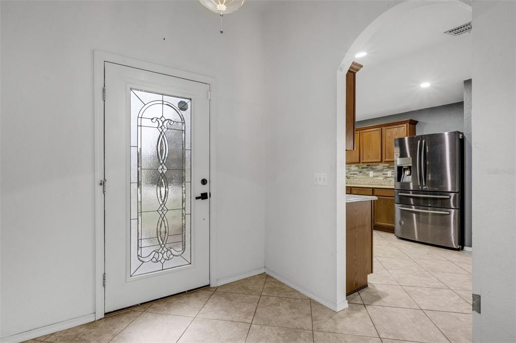 An entryway with tile flooring leads to a kitchen featuring wood cabinets and stainless appliances — 1712 CHARMI DRIVE, LAKELAND, FL