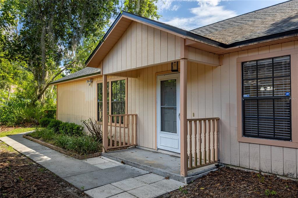 A tan house exterior features a covered front porch with wooden railings and a walkway — 2951 SW 40TH AVENUE, GAINESVILLE, FL