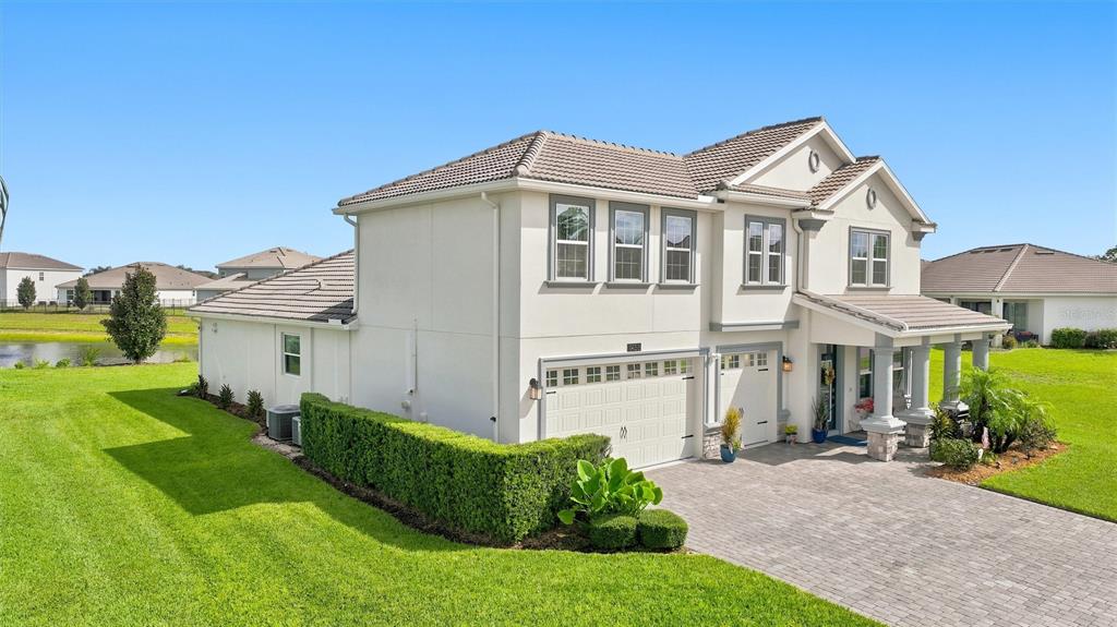 A two-story suburban house with a paved driveway, a manicured hedge, and a side pond — 1458 OLYMPIC CLUB BOULEVARD, DAVENPORT, FL