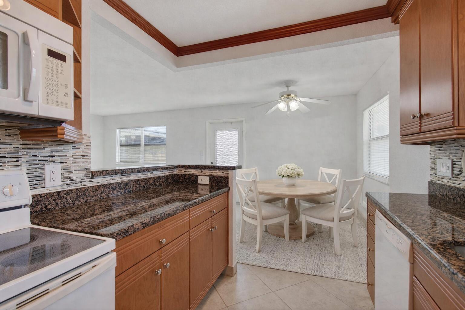 A kitchen with brown granite countertops and wood cabinets overlooks a dining area with seating — 228 Brittany E, Delray Beach FL 33446, DELRAY BEACH, FL