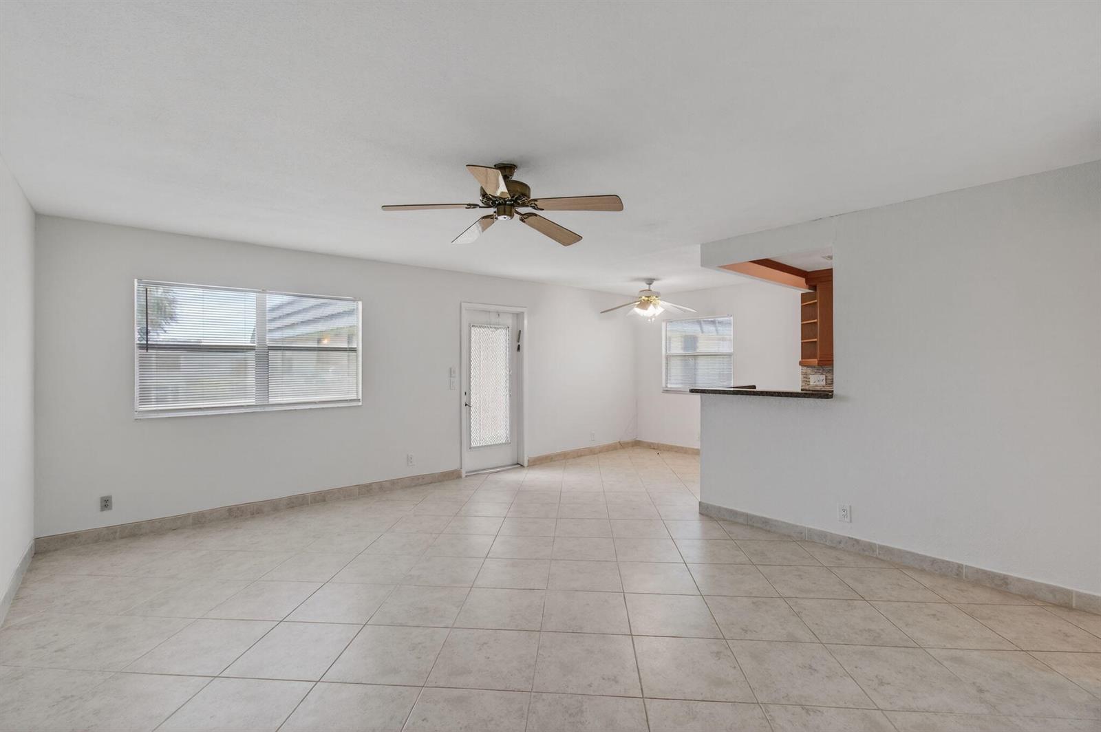 An open-concept living area features light-colored tile flooring, white walls, and two ceiling fans — 228 Brittany E, Delray Beach FL 33446, DELRAY BEACH, FL